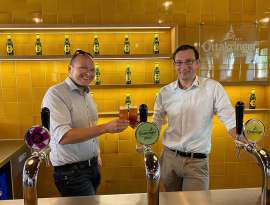 Micke Neureiter und Tobias Frank stossen mir einem Bier vor einer gelben Wand mit Ottakringer Logo und Flaschen an