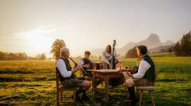 Bauernherbst: Ein Quartett in Tracht spielt auf einer Wiese vor einem Sonnenuntergang