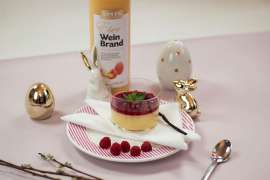 Österliche Panna Cotta mit Spitz Eierweinbrand inmitten österlicher Dekoration, dahinter die Flasche