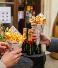 Am mercato Barbaro halten zwei Hände je ein Papierstanizel mit Essen, dahiner zahlreiche Flaschen Moet & Chandon