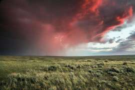 Bedrohliche feuerrote Wolken mit Blitzen über einer Wiese
