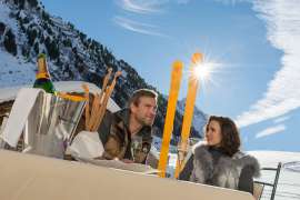 Champagnergenuss auf der Sonnenterrasse, im Hintergrund schneebedeckte Berge unter strahlend blauem Himmel