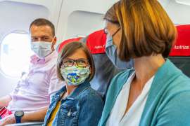 In einem Flugzeug sitzen ein Mann, ein Kind und eine Frau, alle drei mit MNS-Masken