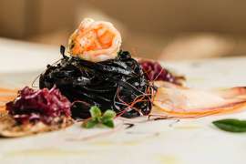 Ein raffinierte angerichteter Meeresfrüchteteller, im ZTentrum ein Knäuel schwarze Nudeln, gekrönt von einem zartrosa Scampi