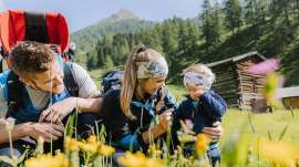 Eine Familie mit Kind in einer Bergwiese, dahinter hohe Berge