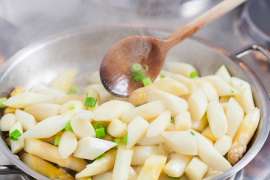 Weisser Spargel wird mit Frühlingszwiebelringen in der Pfanne angeschwenkt