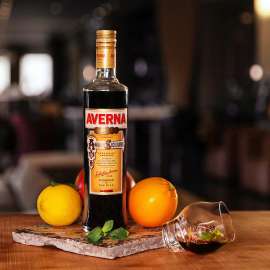Eine Flasche Averna, links davor eine Zitrone, rechte eine Orange sowie ganz rechts ein Glas Averna