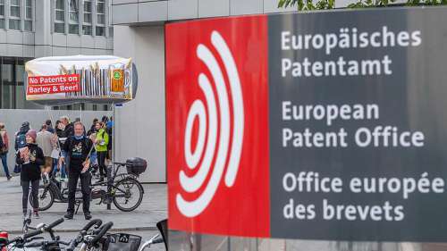 Rechts vorne im Bild Logo und Schriftzug 'Europisches Patentamt', links dahinter Protestierende mit Postern gegen Patente auf Braugerste 