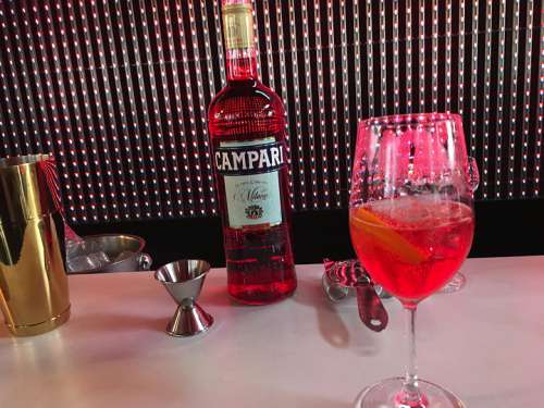 Auf der Bartheke vor dem Kameel stehen Barutensilien, eine Campariflasche und ein Glas Spriti