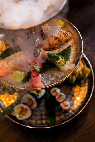 Zwei runde Platten mit kreativem Sushi in der Etagere, darüber eine Platte mit Trockeneis