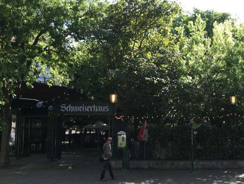 Zwischen grünen Bäumen der Eingang zum Schweizerhaus mit Schild