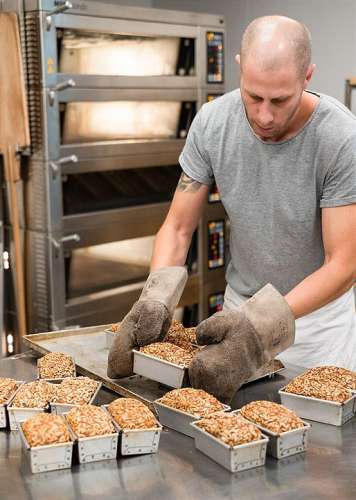 Joseph Weghaupt vor dem Backofen mit mehreren Formen mit glutenfreies Bio Saaten Brot