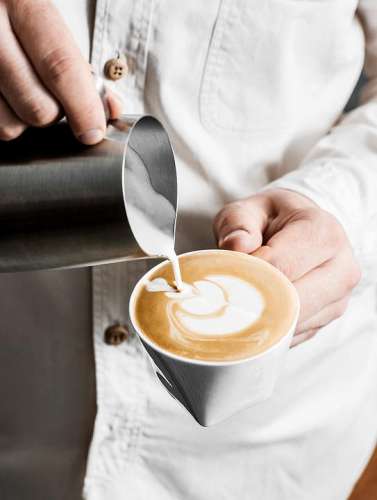 Ein Barista giesst aufgeschäumte Milch zum Espresso und erzeugt damit ein hübsches Muster auf der Oberfläche
