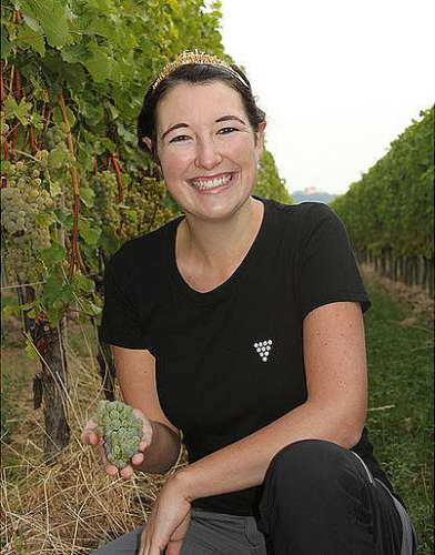 Die Pfälzische Weinkönigin Anna-Maria Löffler vor Weinstöcken mit einer perfekt reifen Weissweintraube in der Hand