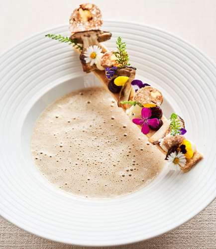Ein Teller Steinüilzcremesuppe mit bunten Blüten dekoriert