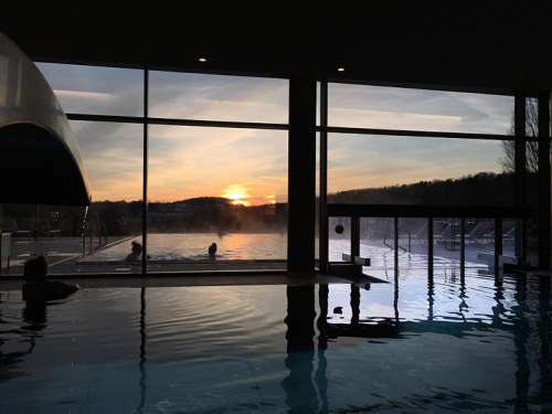 Die anbendliche Poollandschaft des Falkensteiner Balance Hotel Stegersbach, im Hintergrund ein farbenfroher Sonnenuntergang