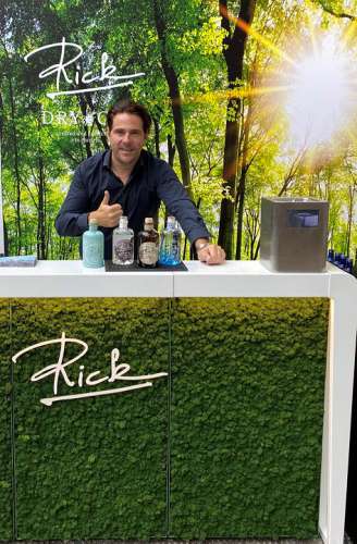Das Rick Gin Sortiment auf einem weissen Tisch, dahinter Patrick Marchl, im Hintergrund ein Birkenwald